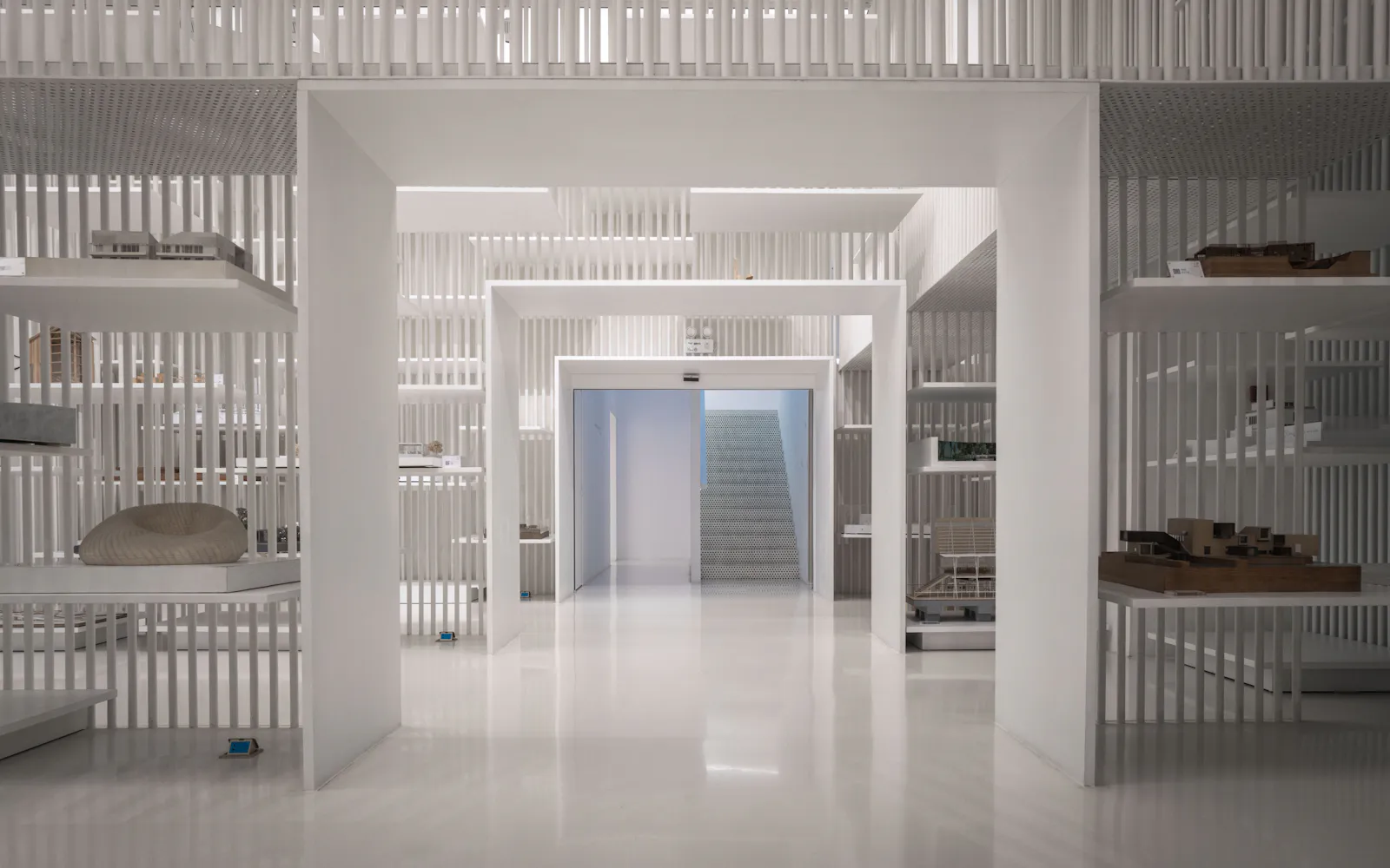 Espacio expositivo blanco con volúmenes y estanterías de líneas arquitectónicas