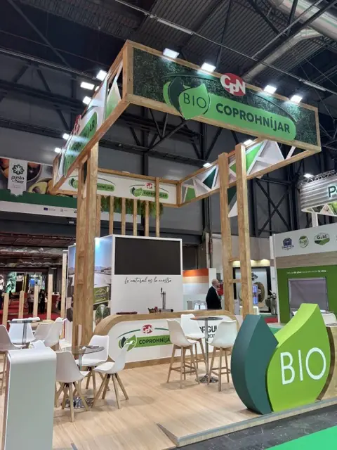 Stand de Coprohnijar con estructura de madera, banderola vegetal y zona de mesas